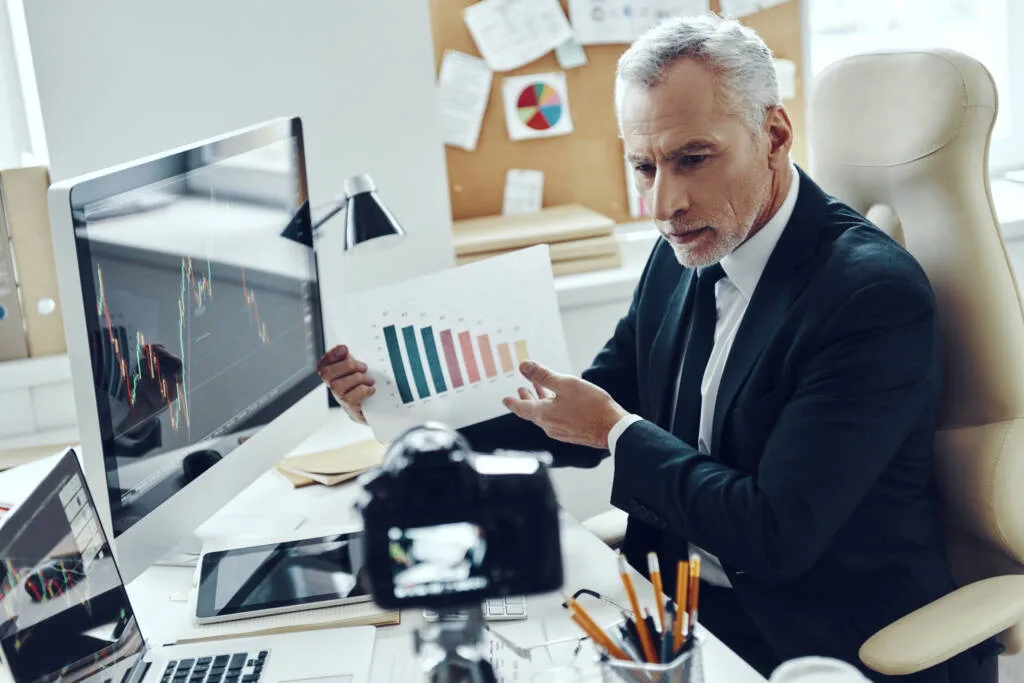 Senior man in elegant business suit showing graph while making social media video